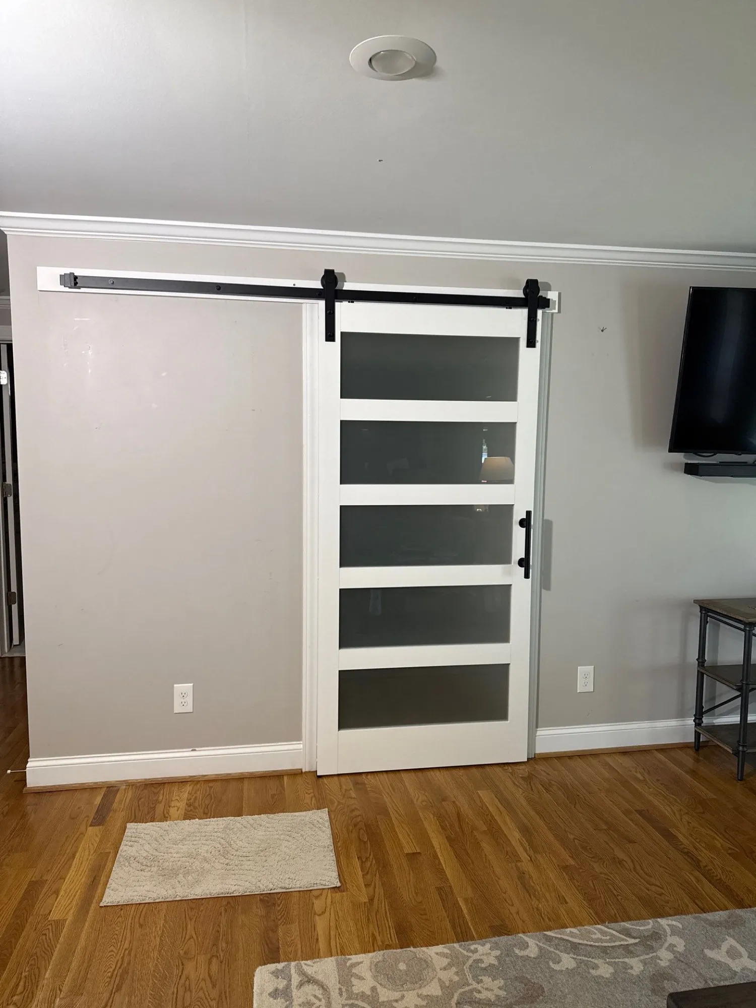 White sliding barn door hung on a black wall-mounted track, with a wall-mounted television on the next wall