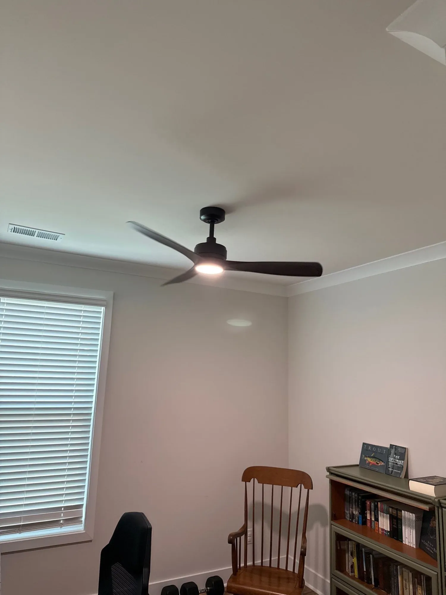 Black three-blade ceiling fan with its light on, hung on a short downrod from a ceiling