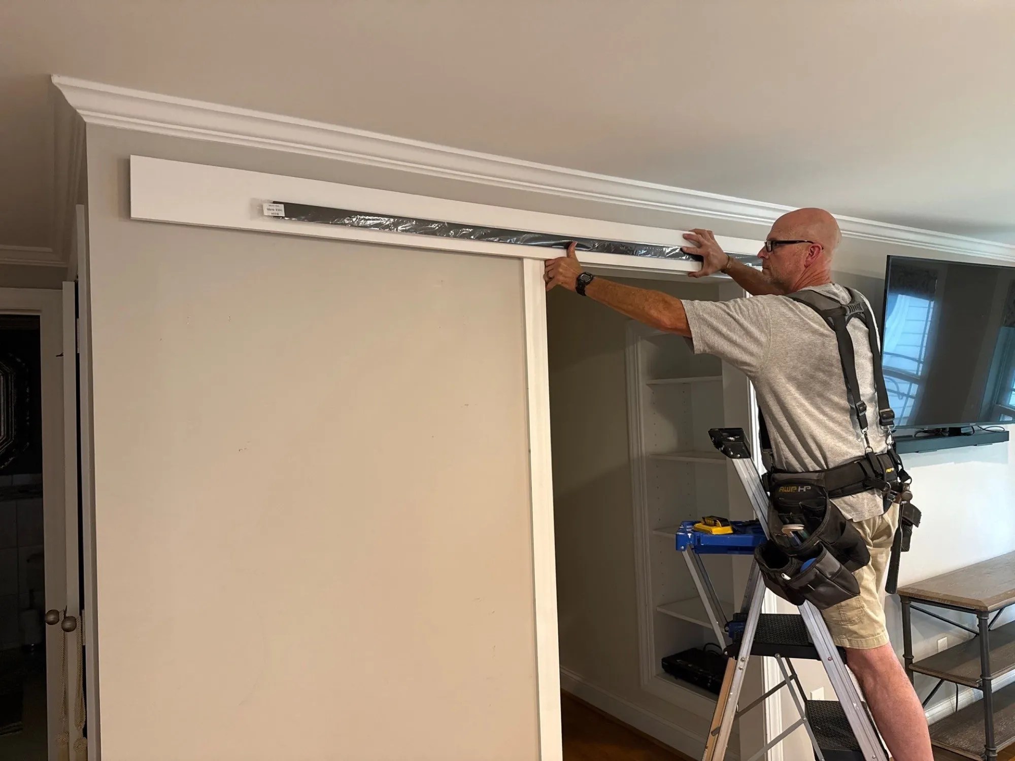 Clay Bucy in a tool harness holding a sliding barn door track against a wall header